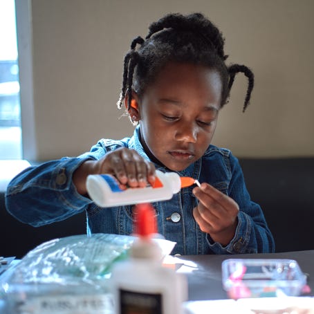 A toddler girl works on an art project with a bottle of glue.