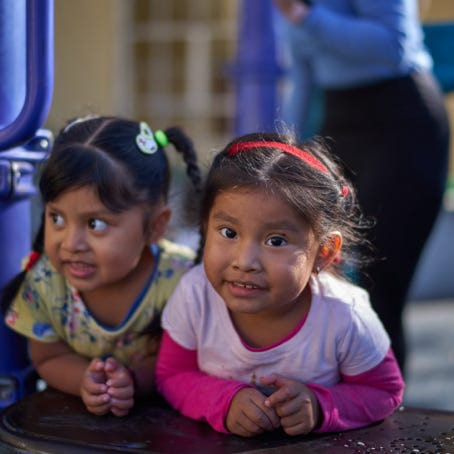 Two little girls look toward the camera at an outdoor event hosted by San Antonio Family Resource Center.