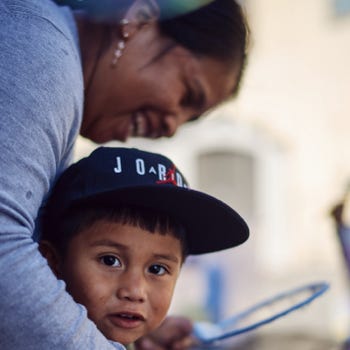 A little boy looks toward the camera as his mom embraces him during an outside event with San Antonio Family Resource Center.