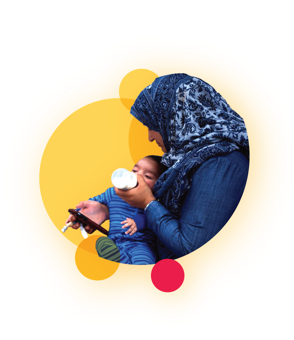 A woman wearing a hijab feeds her baby with a bottle.